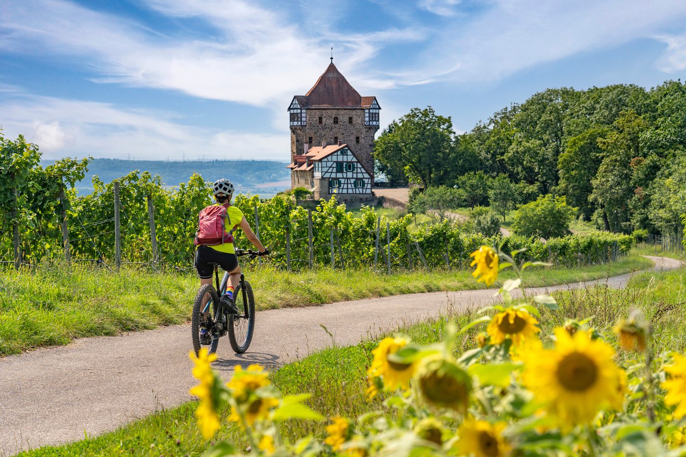 Ciclista pedalando em direção a um castelo entre vinhedos
